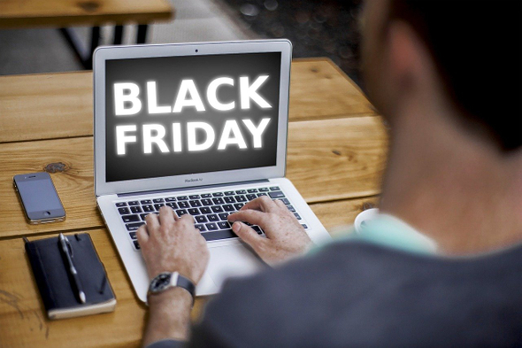 A imagem mostra um homem de costas. Ele está sentado em frente ao computador e na tela é possível ver o termo Black Friday.