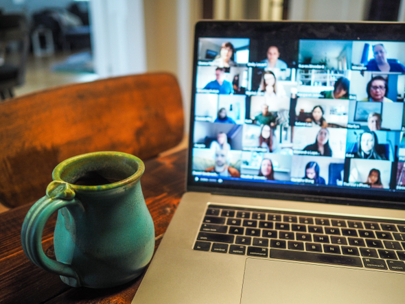 Um notebook aberto em uma reunião por vídeo chamada, a tela está um pouco desfocada e ao lado, está uma caneca de café.