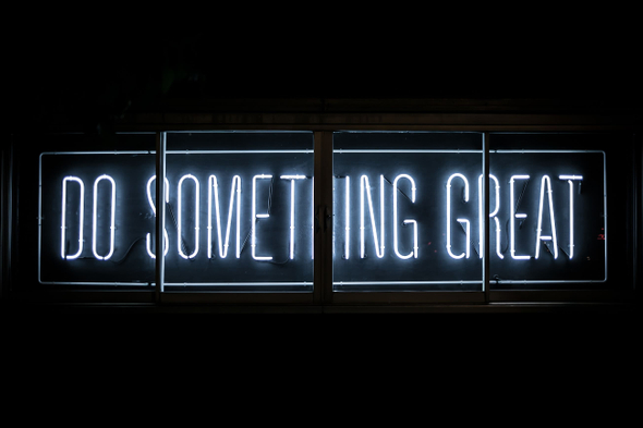 Num ambiente escuro, um letreiro eletrônico de néon com os dizeres: “do something great”.